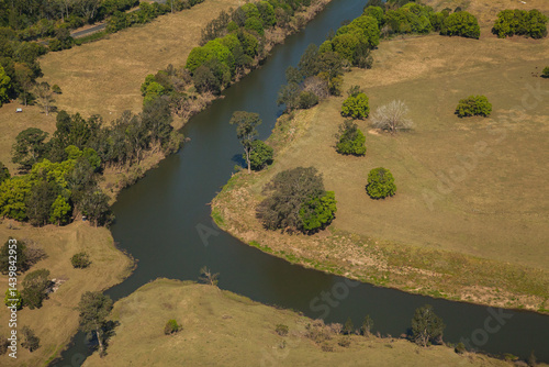 Aerial of tree lined river bend beside farms
