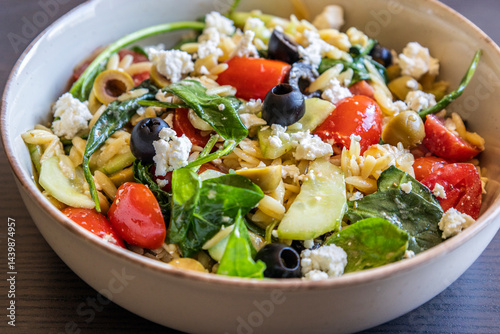  healthy orzo salad served in a bowl, made with fresh vegetables, black olives, and crumbled feta cheese close up