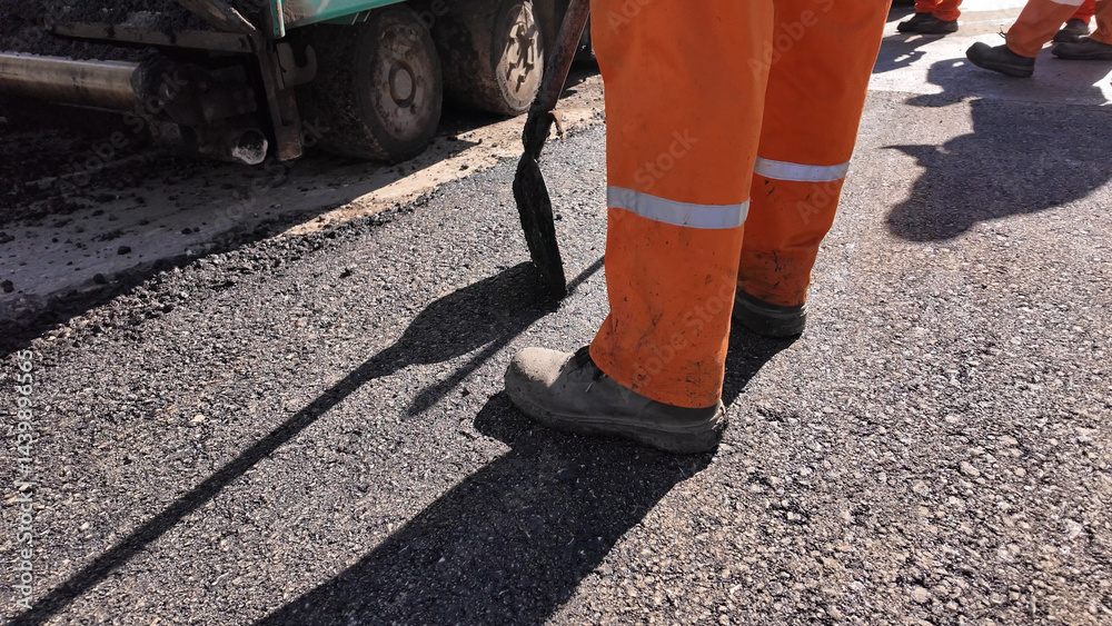 Construction workers working on a new asphalt layer on a public street.
