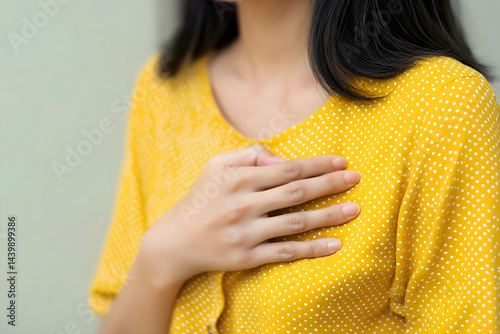 A woman in a yellow polka dot shirt places her hand over her chest, suggesting emotion or concern.