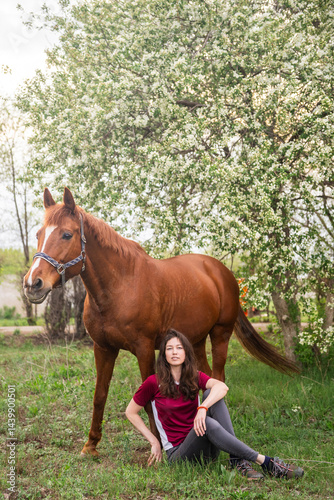 A female horse owner and a thoroughbred mare on the background of a blooming apple tree photo