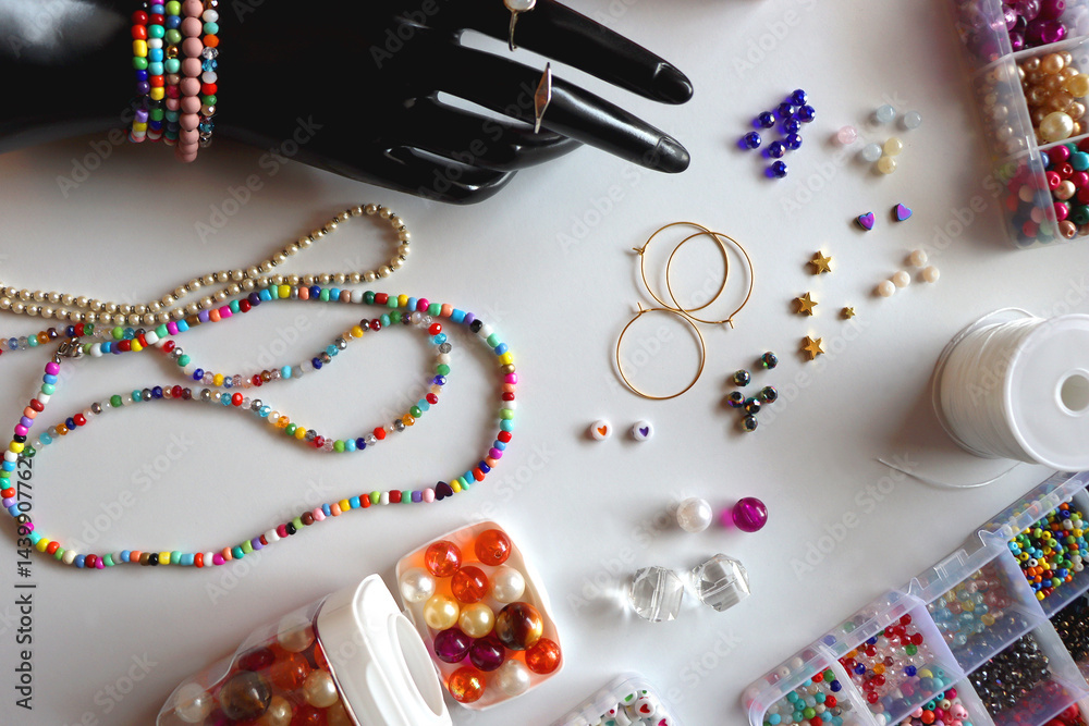 Hand figurine, colorful friendship bracelets, necklaces, various beads and DIY supplies on the table. Making jewelry at home. Flat lay.