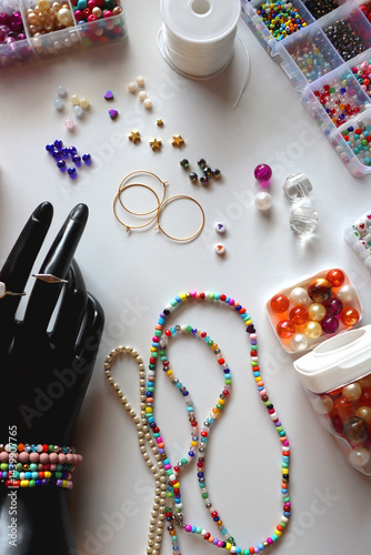 Hand figurine, colorful friendship bracelets, necklaces, various beads and DIY supplies on the table. Making jewelry at home. Flat lay.