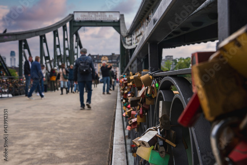 Obraz na płótnie The Eiserner Steg bridge in Frankfurt, Germany, features colorful love locks on its green metal railings, with the city skyline visible under a cloudy sky. w salonie