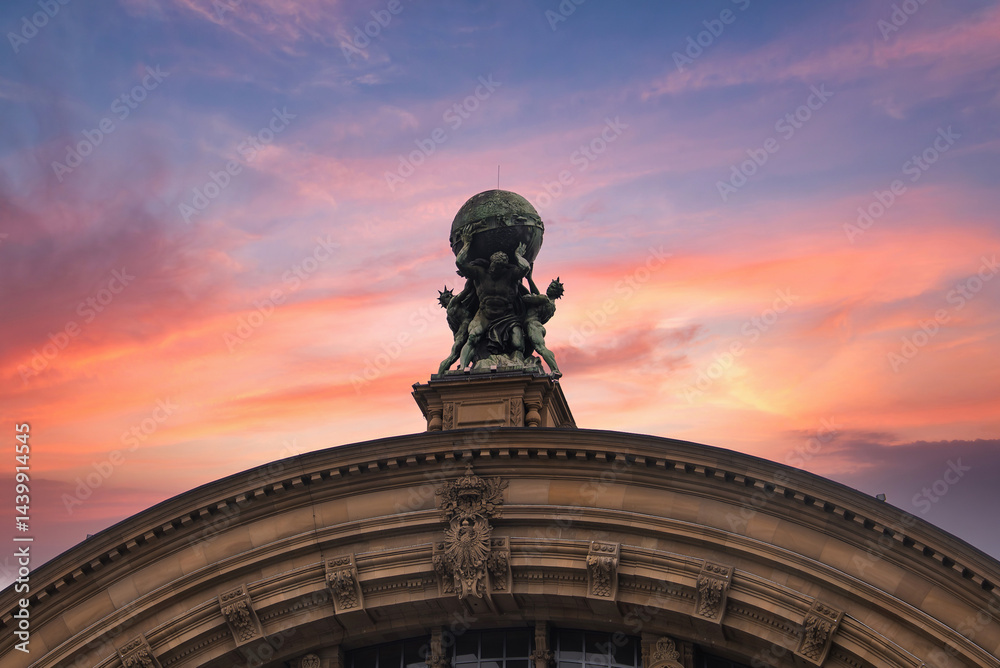 The ornate facade of Frankfurt Central Station in Germany features a bronze Atlas sculpture with intricate carvings under a cloudy sky.