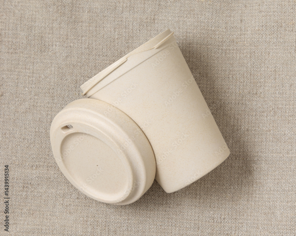 Opened beige reusable bamboo coffee cup on beige linen cloth top view, copy space, mockup