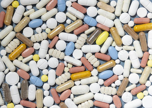 Pile of mixed white, yellow and blue medical capsules and pills on blue top view