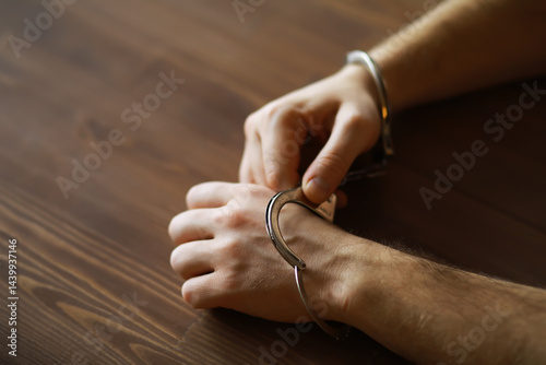 Obraz na płótnie Closeup of Hands in Handcuffs on Wooden Table - Arrest, Detainment, and Justice Symbolism w salonie