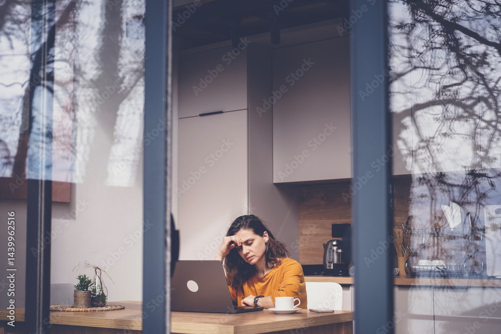 Serious thoughtful sad woman sitting at home working on laptop