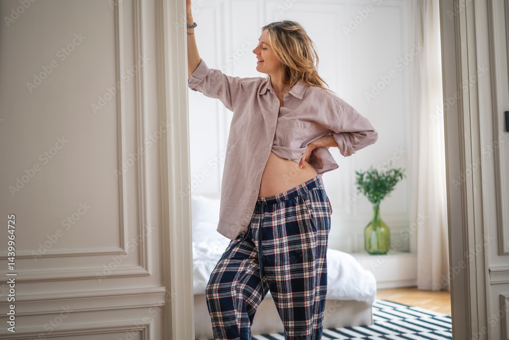 Pregnant woman with hands on stomach standing in apartment