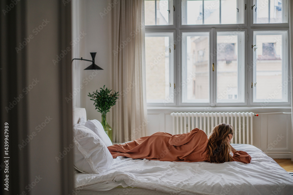 Woman lying on bed in bedroom with window