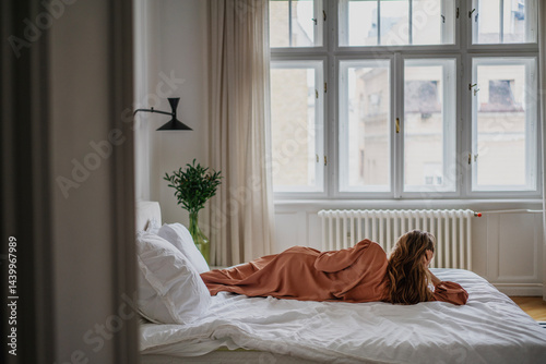 Woman lying on bed in bedroom with window