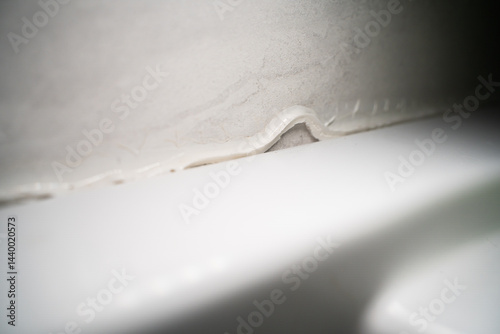 Poor quality white sealant in shower stall close-up. Removing sealant to replace and applying fresh sealant to protect against moisture