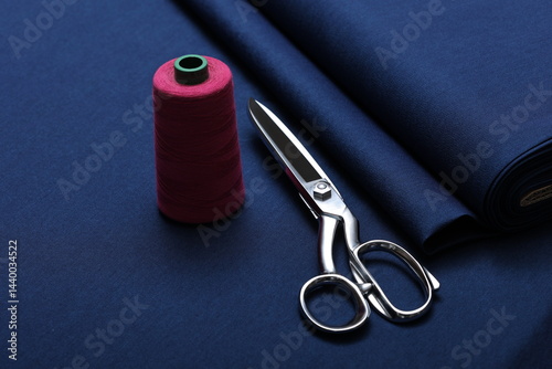 Professional sewing scissors rest atop a bolt of deep blue denim fabric, representing craftsmanship, fashion tailoring, and precision in garment-making.