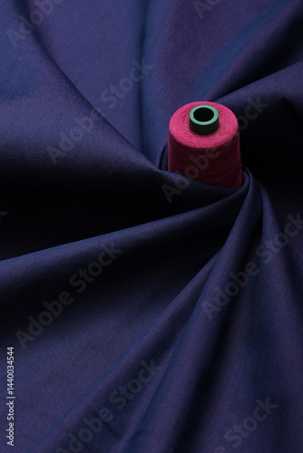 Sewing thread rest atop of a deep blue denim fabric, representing craftsmanship, fashion tailoring, and precision in garment-making.