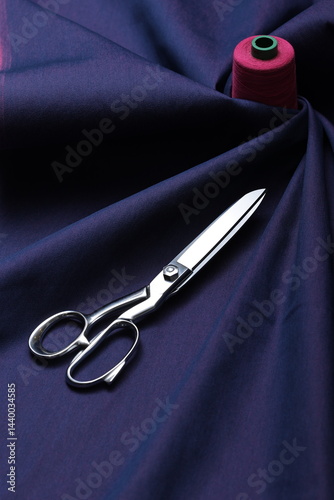 Professional sewing scissors rest atop a bolt of deep blue denim fabric, representing craftsmanship, fashion tailoring, and precision in garment-making.