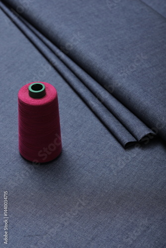 Sewing thread rest atop of a deep blue denim fabric, representing craftsmanship, fashion tailoring, and precision in garment-making.