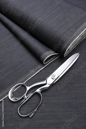 Professional sewing scissors rest atop a bolt of deep blue denim fabric, representing craftsmanship, fashion tailoring, and precision in garment-making.