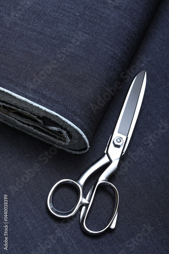 Professional sewing scissors rest atop a bolt of deep blue denim fabric, representing craftsmanship, fashion tailoring, and precision in garment-making.