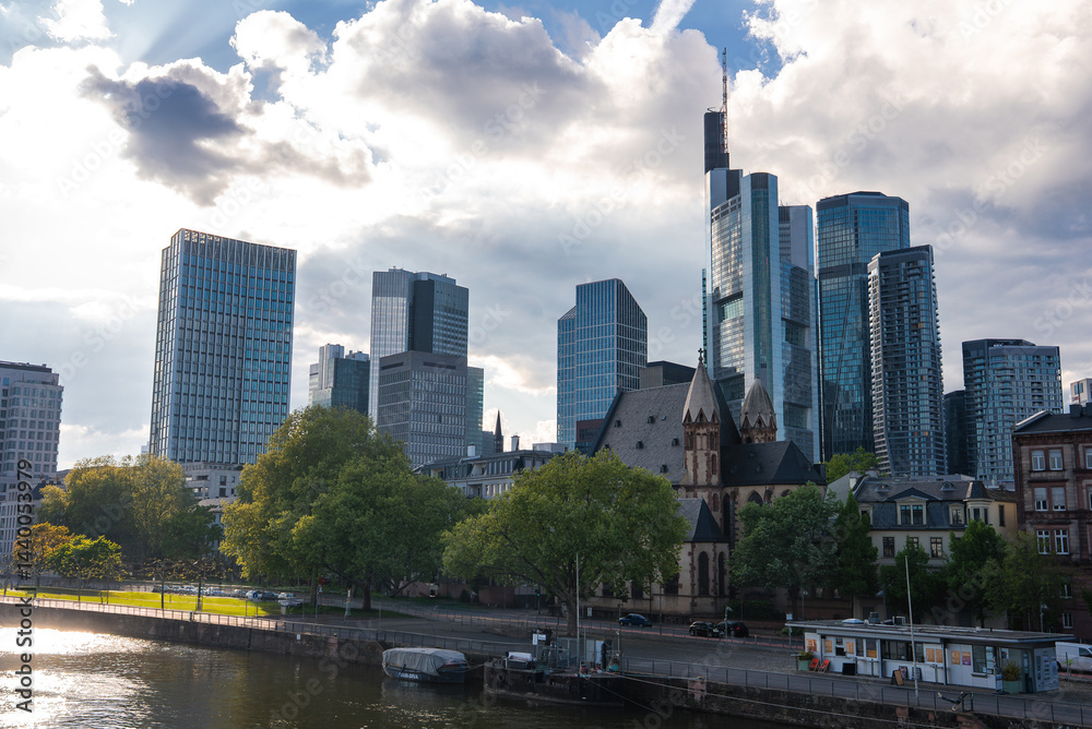 Skyline of Frankfurt, Germany, featuring Main Tower, modern skyscrapers, a historic church, European style buildings, and the Main River with a promenade.