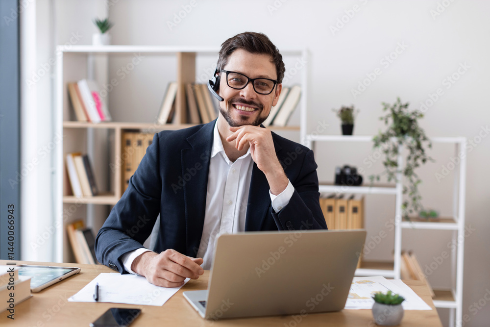 Smiling adult male wearing suit using laptop during business communication in office setting. Smiling adult male wearing suit using laptop during business communication in office setting.