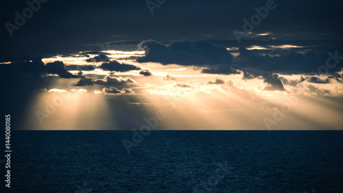 Beautiful sunset over the ocean with rays of sunlight piercing through dark clouds in the evening sky