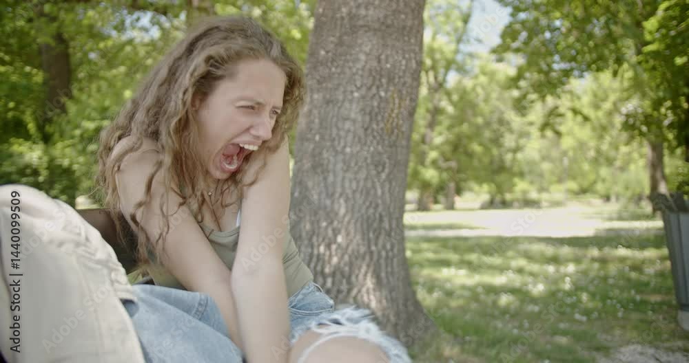 A young woman sits on a park bench, experiencing a sudden onset of intense fear or panic. She cries and clutches her knees. A young woman sits on a park bench, experiencing a sudden onset of intense fear or panic. She cries and clutches her knees.