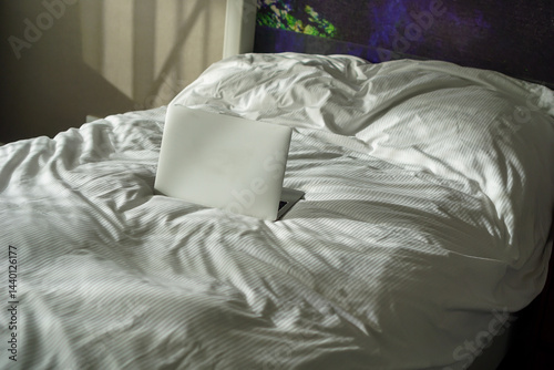 Open laptop on a white bed, working from home, remote work, laying down in comfort, cozy workspace, concept of productivity, modern lifestyle, home office setting photo