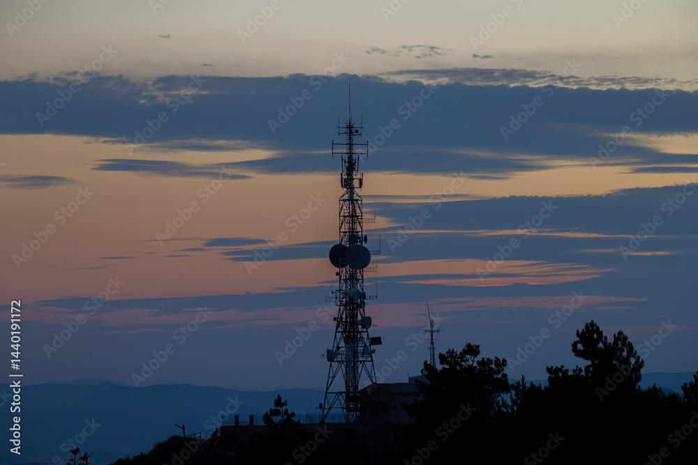 Telecommunication tower silhouette at sunset illuminating colorful clouds