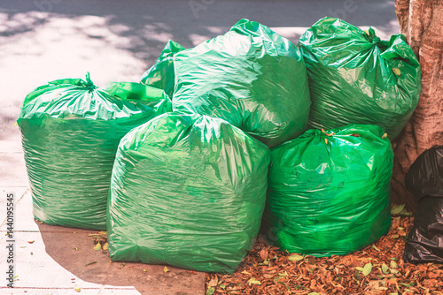 Obraz na płótnie Overflowing green garbage bags are situated on a paved surface, amongst fallen leaves. Full refuse bags, tied rest on the ground w salonie