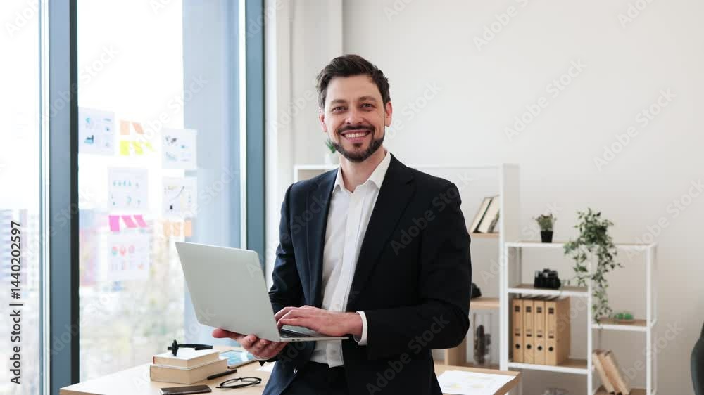 Smiling male business professional in modern office with laptop, wearing formal attire, expressing confidence and success. Young adult man, medium build, standing by desk with organized workspace Smiling male business professional in modern office with laptop, wearing formal attire, expressing confidence and success. Young adult man, medium build, standing by desk with organized workspace