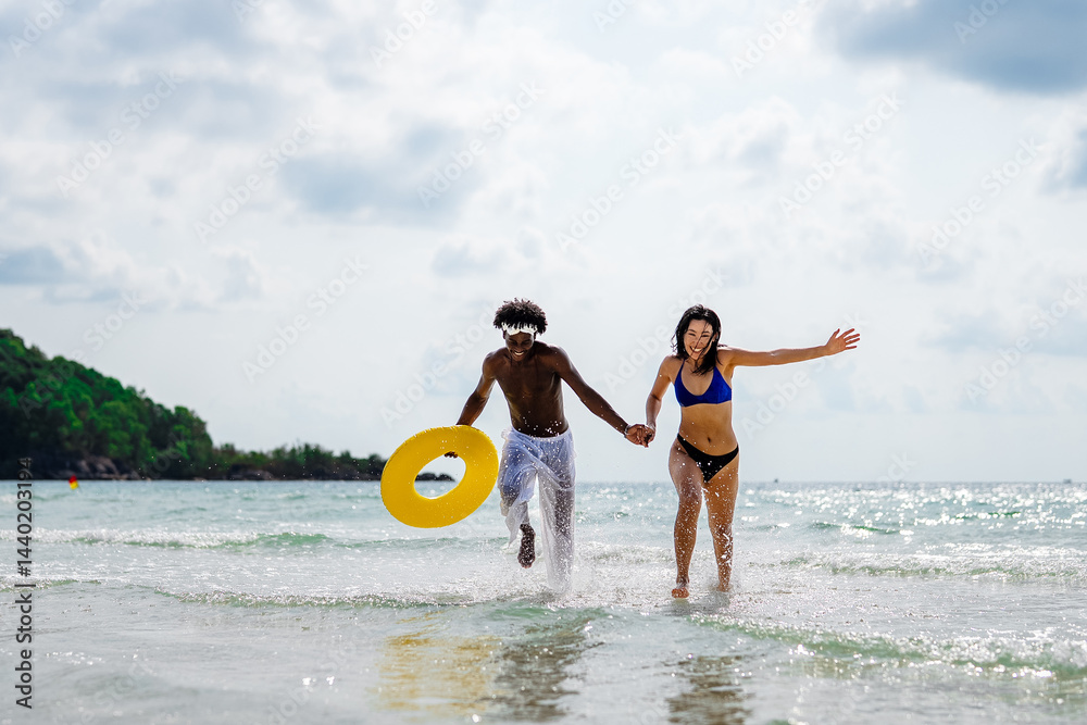 Happy interracial couple enjoying a fun beach day, splashing in the ocean waves, holding hands
