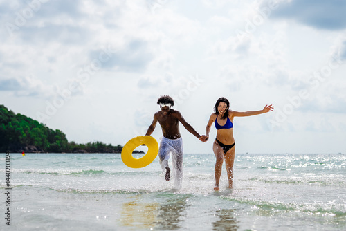 Obraz na płótnie Happy interracial couple enjoying a fun beach day, splashing in the ocean waves, holding hands w salonie