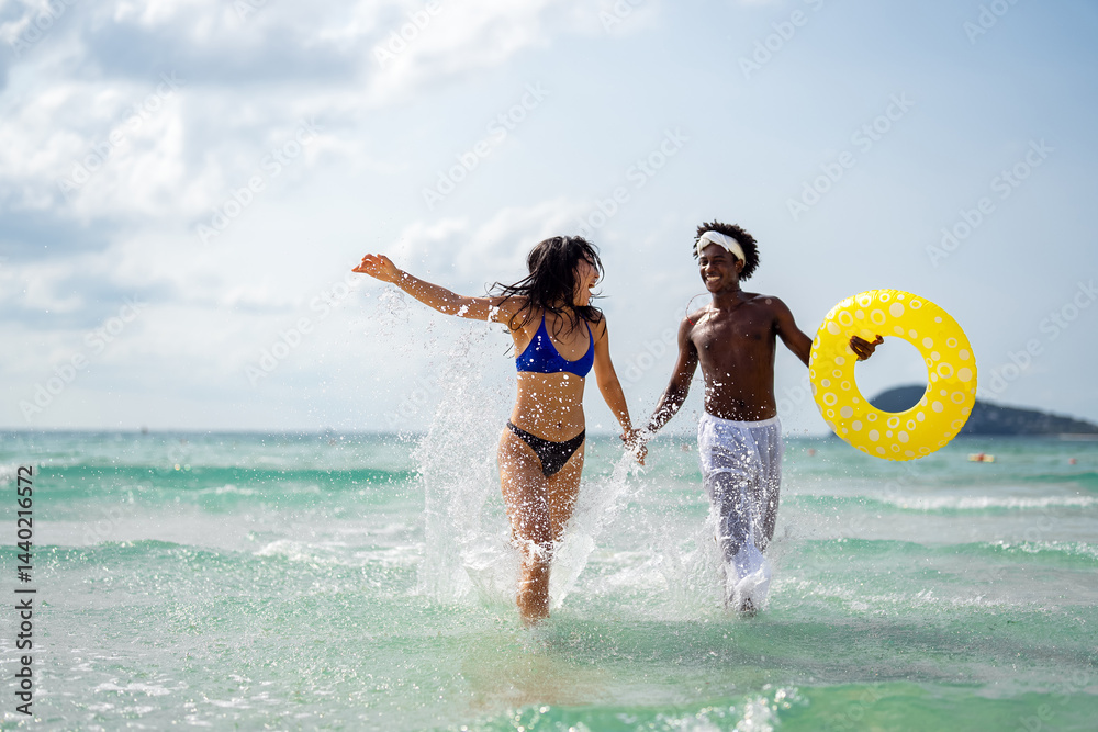 Interracial couple having fun at the beach, running through ocean waves on a tropical vacation