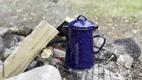 Blue enamel coffee pot sits on a grill over a fire with wood, camping, outdoor cooking and rustic adventure, cozy ambiance