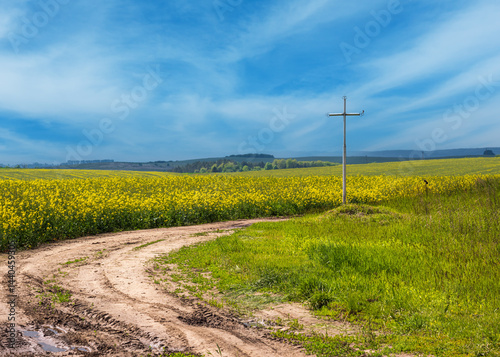 Obraz na płótnie Spring rapeseed yellow blooming fields and religious cross near the pass w salonie