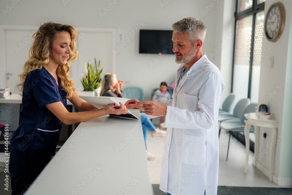 Obraz premium Doctor and nurse discussing important details at the reception desk of a modern hospital clinic, while patients wait in the background, creating a dynamic healthcare environment