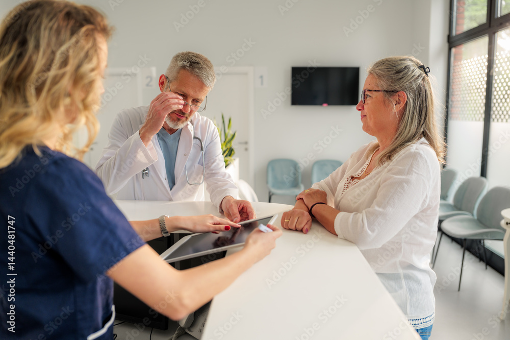 Fototapeta premium Doctor and nurse are sharing test results with a concerned senior patient on a digital tablet in a bright hospital waiting room, discussing diagnosis and treatment options