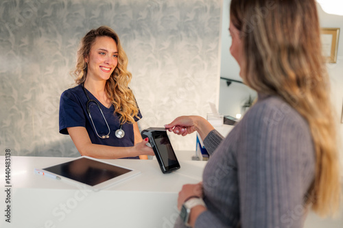 Tablou pe pânză Smiling doctor accepting contactless payment from female patient at modern clini