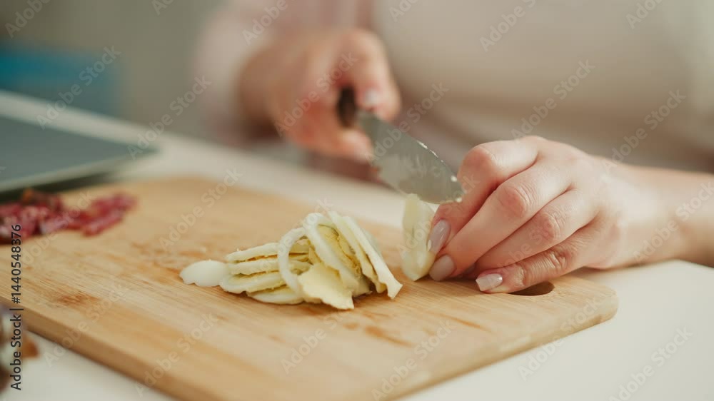 Hands of creative slicing boiled egg into thin round shapes on wooden cutting board beside cured sausage slices under natural light, showcasing precise kitchen technique and elegant appetizer prep