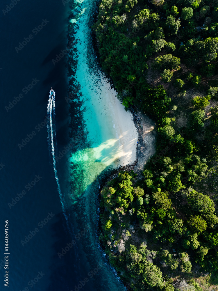 Aerial view of tropical coastline in Thailand, with a speedboat cutting through deep blue waters near a lush green island.
