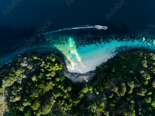Drone shot of a boat cruising past a hidden beach in Thailand, surrounded by dense green jungle and vibrant blue waters.