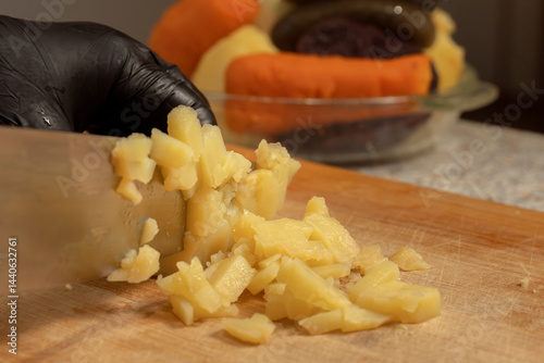 Chef cutting boiled potatoes for salad on a cutting board against the background of other vegetables. Close-up. Cooking