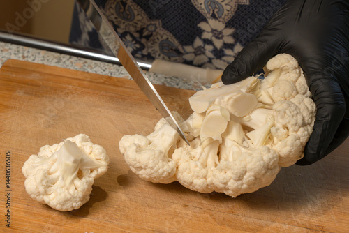 Chef cuts a head of cauliflower into florets on a kitchen cutting board. Close-up