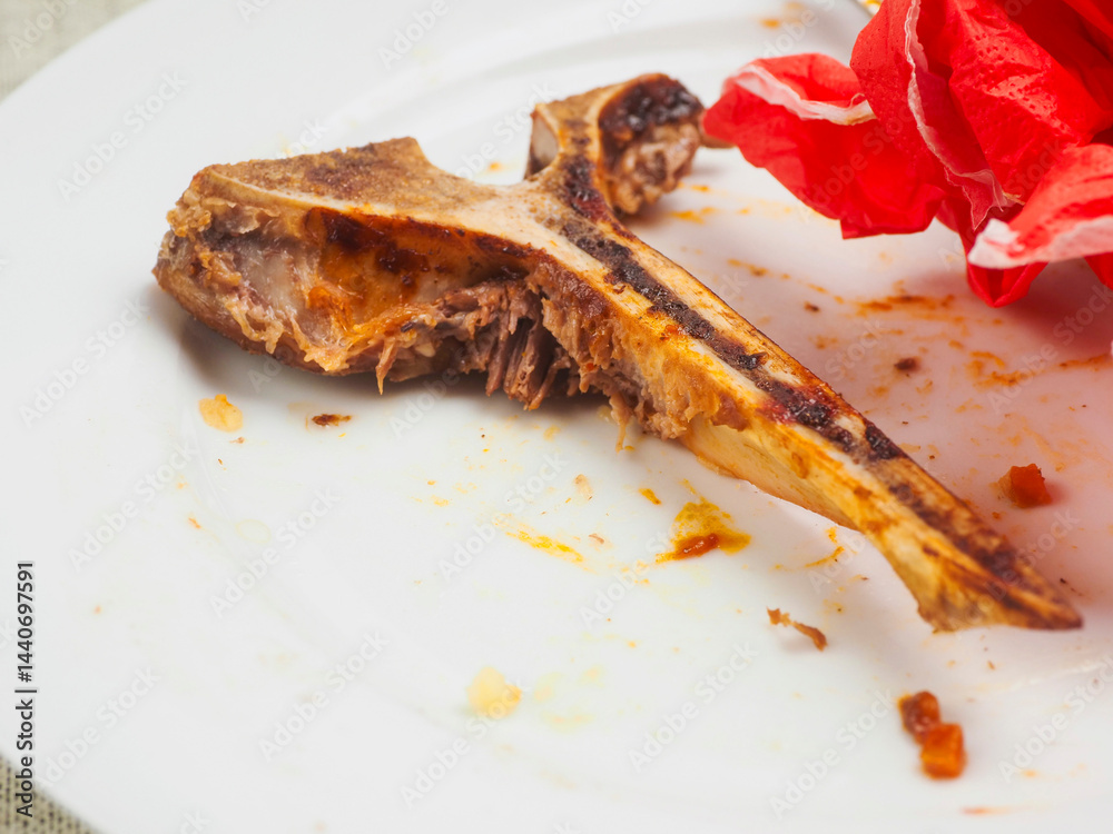 Finished high quality meal. Empty dirty plate with t bone, fork, knife and red napkin on white table cloth. Fine dinner concept. Scraps on a plate.