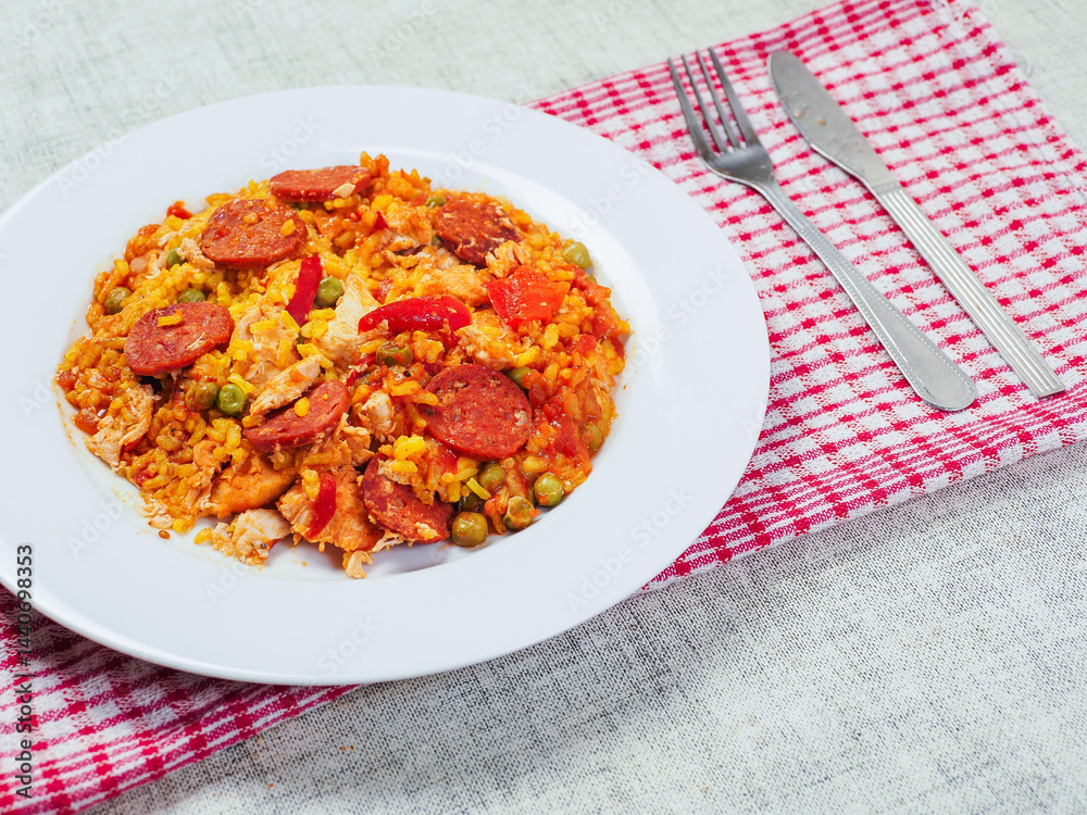 Fine tasty Spanish paella dinner with rice and high quality chorizo sausage on white plate and simple table runner. Mediterranean style dish. Popular food made from premium ingredients.