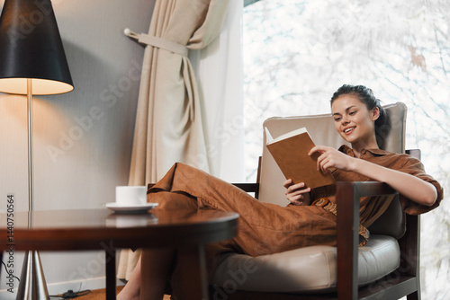 A serene young woman enjoying a cozy reading moment at home, dressed in a stylish brown outfit, conveying relaxation by a lamp with a warm ambiance photo