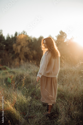 Young woman walking in a field at sunset touching tall grass enjoying nature