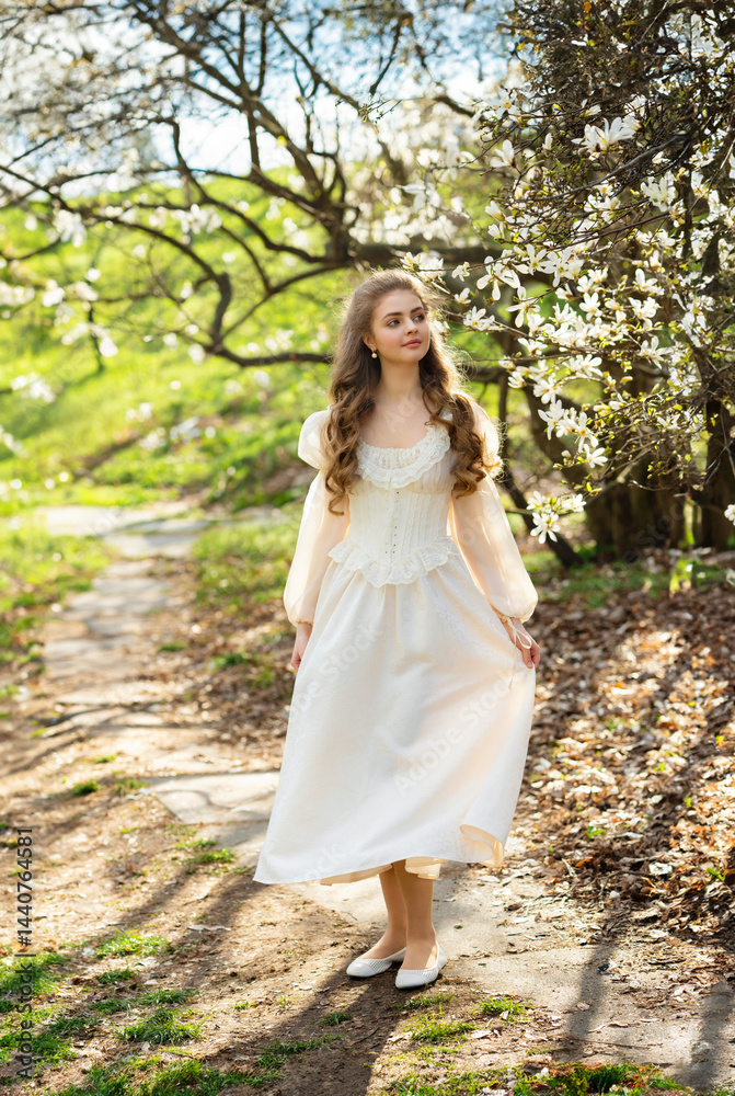 Young blonde curly woman walking in a blooming magnolia garden. Springtime, natural beauty, soft sunlight, romantic and peaceful atmosphere. Fine art style portrait in nature. Young blonde curly woman walking in a blooming magnolia garden. Springtime, natural beauty, soft sunlight, romantic and peaceful atmosphere. Fine art style portrait in nature.