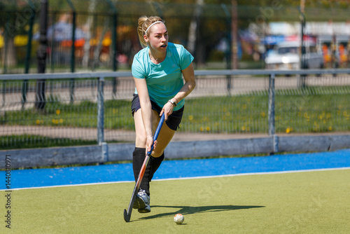 Young sportswoman leading the ball at the field hockey game